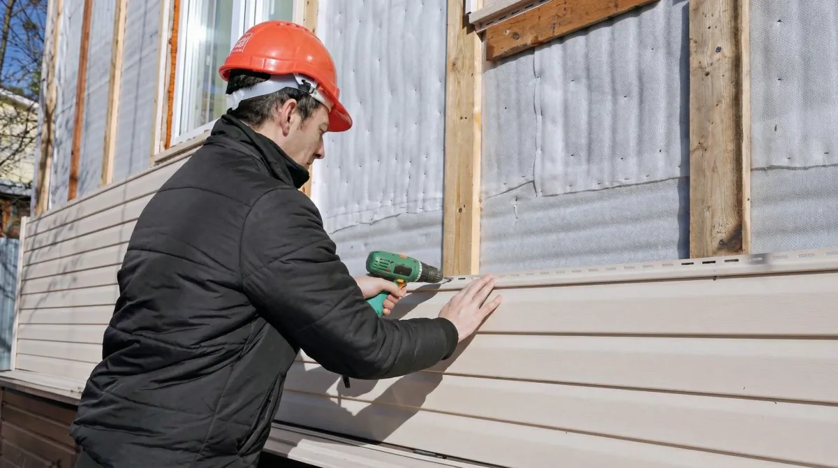 Siding replacement professional using a power drill to install new tan vinyl siding on a home exterior in Bradenton, FL